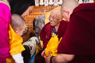 The compassion and wisdom of His Eminence Luding Khenchen Rinpoche emanates from his smile as he offers little Thugsey and Sangyumla a Buddha